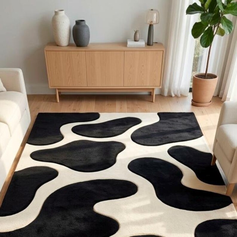 May include: A rectangular area rug featuring a high-contrast pattern of large, irregular black organic shapes set against a solid cream-colored background. The rug has a plush, textured surface and covers a significant portion of the floor space.
