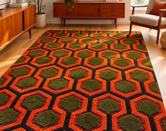 May include: A rectangular area rug featuring a repeating geometric pattern of dark olive green hexagons outlined by thick, vibrant orange borders and thin black lines. The rug has a textured pile surface and covers a light-colored wooden floor.