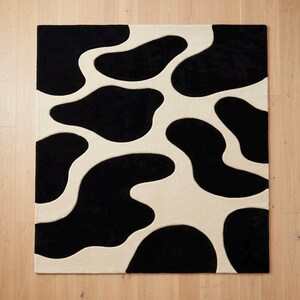 May include: A rectangular area rug featuring a high-contrast pattern of irregular, organic black shapes set against a solid cream-colored background. The design creates a fluid, abstract aesthetic with deep pile texture throughout the entire surface.