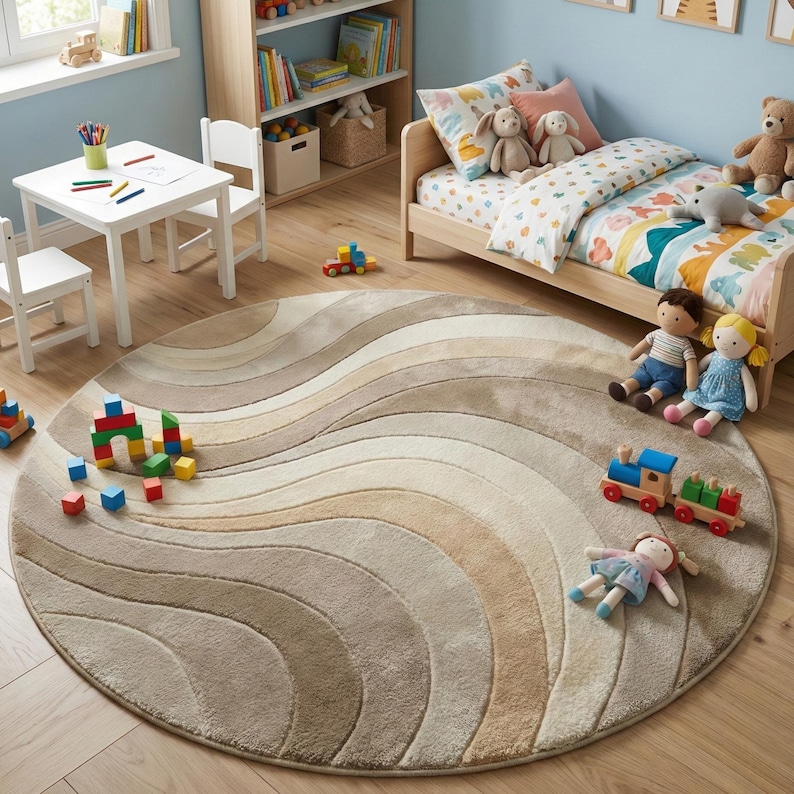 May include: A round rug with a wavy pattern in shades of beige, tan, and cream. The rug is in a child's bedroom, with toys and furniture visible. The rug is a soft, neutral accent piece.