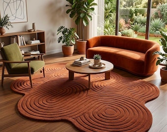 May include: A large, rust-colored area rug with a distinct, organic, cloud-like shape and a textured, concentric swirl pattern. The rug is placed on a wooden floor, featuring deep, carved lines that create a repeating circular motif throughout.