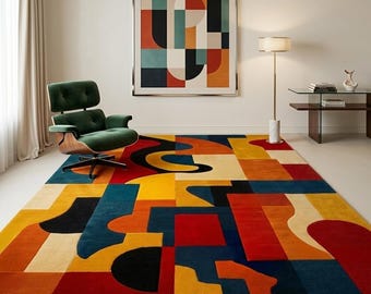 May include: A large rectangular area rug featuring a bold geometric pattern in vibrant shades of red, orange, yellow, teal, and black. The rug covers the floor, complementing a green lounge chair, a floor lamp, and a framed wall art piece.