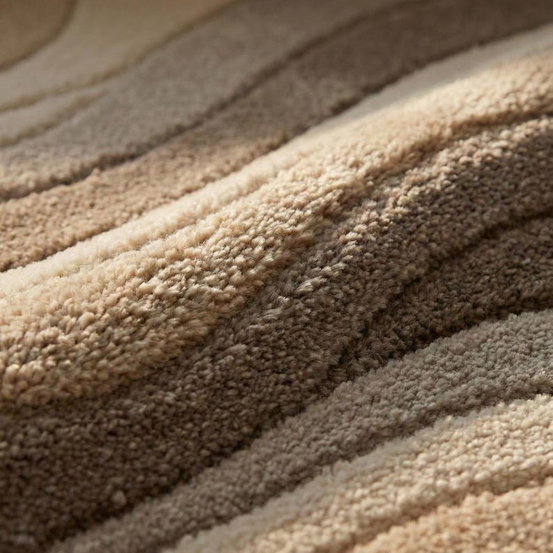 May include: Close-up of a plush rug with a striped pattern. The rug features alternating bands of beige, tan, and brown, creating a textured, layered effect. The soft, fluffy material suggests comfort and warmth, ideal for home decor.