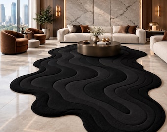 May include: A large, black area rug with an irregular, organic shape featuring deep, flowing wave-like patterns carved into the surface. The rug has a thick, plush texture and covers a significant portion of the light-colored tiled floor.