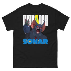 May include: Black t-shirt with a cartoon bat illustration. The bat has red eyes and an open mouth. A bat-like figure in a suit stands beside the bat. The words "DISPATCH" and "SONAR" are printed on the shirt.