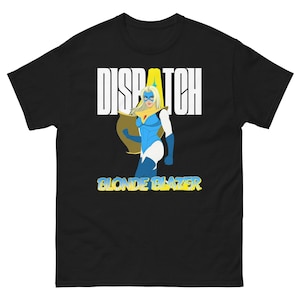 Può includere: T-shirt nera con grafica di supereroina e le scritte "DISPATCH" e "BLONDE BLAZER". L'illustrazione mostra una supereroina bionda in costume blu e bianco con mantello giallo.