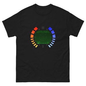 Peut inclure: T-shirt noir avec un motif de cadran de montre, avec un centre vert et des anneaux segmentés colorés. Le texte "G WATCH V2.0 BETA MISSION STATUS: INCOMPLETE" est affiché au-dessus du cadran. Le t-shirt est de style col rond.