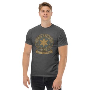 Puede incluir: Camiseta gris oscuro con un emblema circular con una estrella dorada y el texto "FLORIDA BATTALION OF INFANTRY" y "NULLI SECUNDUS". La camiseta es de cuello redondo.