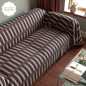 Peut inclure: Housse de canapé à rayures marron et blanches. La housse présente un motif répété de rayures marron et blanches avec un motif ovale. Le logo The Fancy Covers est dans le coin supérieur gauche. La housse est drapée sur un canapé.
