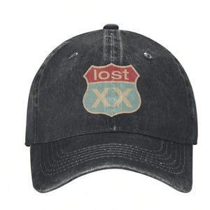 May include: A black denim baseball cap with a curved brim. The cap features a distressed look and a patch on the front with the word "lost" in red, and "XX" in a light green color, set against a light blue background.
