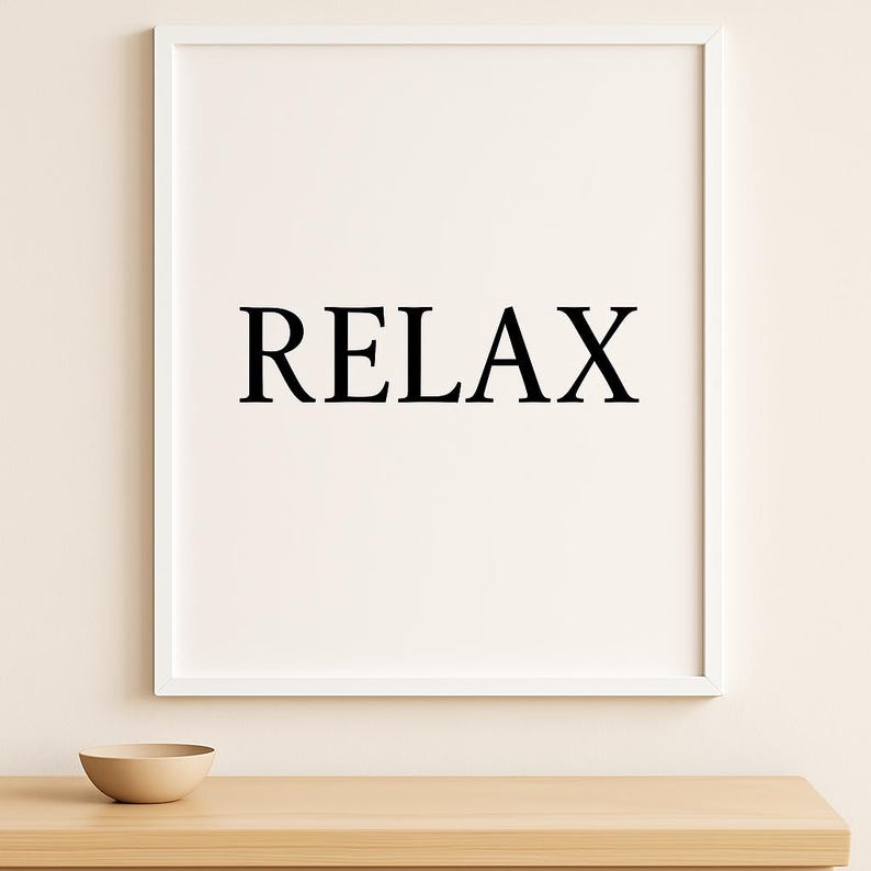 Puede incluir: Un cuadro enmarcado con la palabra "RELAX" en letras negras en negrita centrada sobre un fondo blanco. El marco es blanco, y un peque&ntilde;o cuenco beige descansa sobre una superficie de madera debajo. Tema: decoraci&oacute;n del hogar.