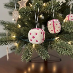 May include: A Christmas tree decorated with ornaments. The ornaments are white cubes with pink polka dots and stripes. Other ornaments include a wooden star and a snowflake. The tree is lit with small white lights.