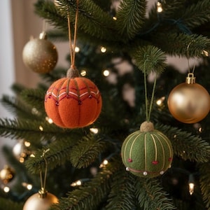 May include: Christmas tree ornaments in various styles. An orange felt ornament with white and red stitching and a green felt ornament with vertical gold lines and small pearls. Gold and bronze spherical ornaments are also visible.