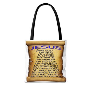 May include: White tote bag with black handles featuring a scroll design. The scroll has the word "JESUS" in blue, with a list of attributes in black text. The bag is designed for carrying items.