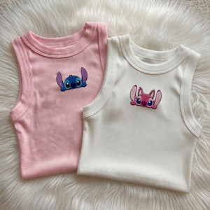 Peut inclure: Deux d&eacute;bardeurs c&ocirc;tel&eacute;s, un rose et un blanc, chacun avec un personnage de dessin anim&eacute; brod&eacute;. Le d&eacute;bardeur rose a un personnage bleu, tandis que le blanc a un personnage rose. Les deux hauts ont un col rond et sont sans manches.