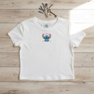 Puede incluir: Camiseta blanca con un bordado del personaje Stitch y corazones rosas. La camiseta de manga corta tiene cuello redondo y est&aacute; hecha de un material suave y ligero. El dise&ntilde;o est&aacute; centrado en el pecho.