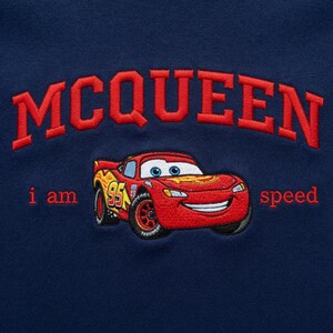 May include: Navy blue sweatshirt featuring an embroidered design. The design includes the word "MCQUEEN" in red, arched across the top, and a red race car with the text "i am speed". The car has the number "95" on the side.