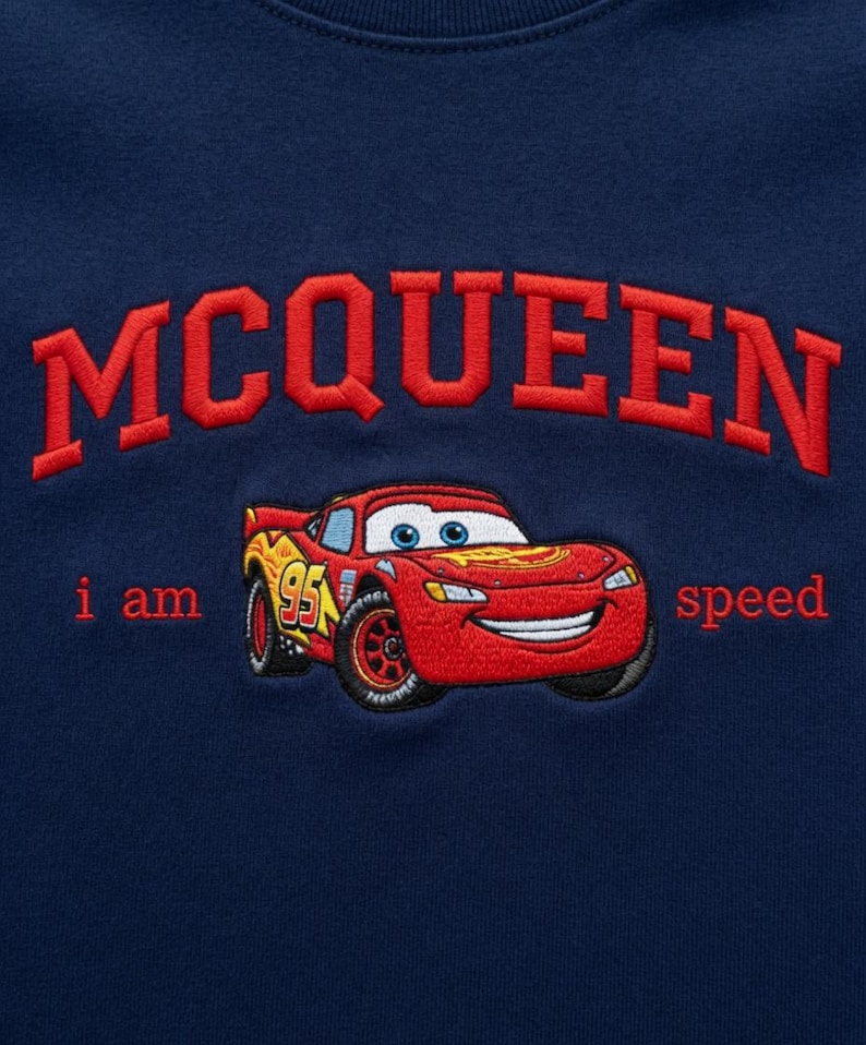 May include: Navy blue sweatshirt featuring an embroidered design. The design includes the word "MCQUEEN" in red, arched across the top, and a red race car with the text "i am speed". The car has the number "95" on the side.