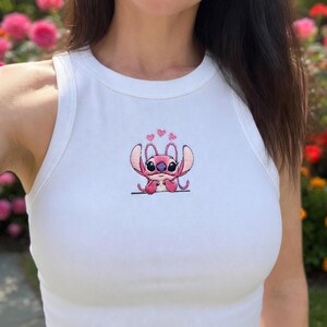May include: White ribbed vest top featuring a pink embroidered cartoon character. The character has large ears, big eyes, and is surrounded by hearts. The vest top is sleeveless with a round neckline.