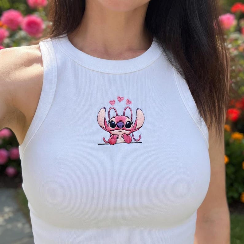 May include: White ribbed vest top featuring a pink embroidered cartoon character. The character has large ears, big eyes, and is surrounded by hearts. The vest top is sleeveless with a round neckline.