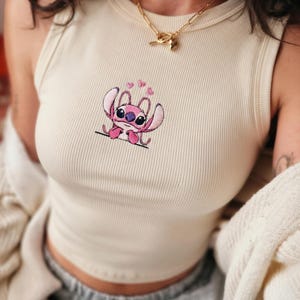 May include: Cream ribbed tank top with an embroidered pink Stitch character and heart details. The vest top has a scoop neck and a fitted shape. A casual, comfortable garment.