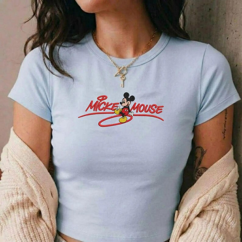 Op de afbeelding: Lichtblauw crop top met de tekst "Mickey Mouse" in rode letters en een cartoonafbeelding van Mickey Mouse. De top heeft korte mouwen en een ronde halslijn.