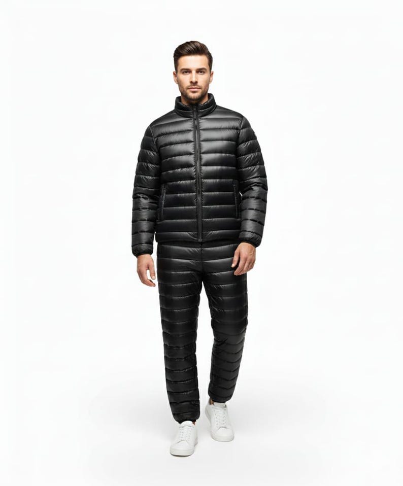 May include: A black, quilted winter suit, including a jacket with a stand-up collar and a full-length zipper, and matching pants. The suit is worn with white sneakers. The outfit is designed for cold weather and outdoor activities.