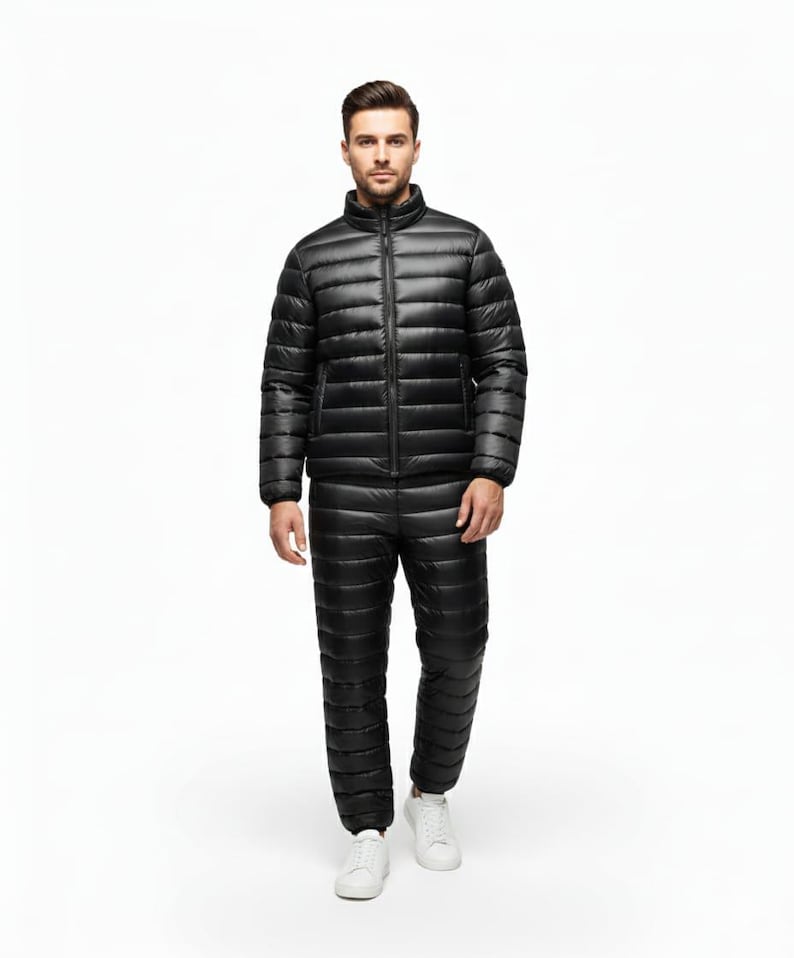 May include: A black, quilted winter suit, including a jacket with a stand-up collar and a full-length zipper, and matching pants. The suit is worn with white sneakers. The outfit is designed for cold weather and outdoor activities.