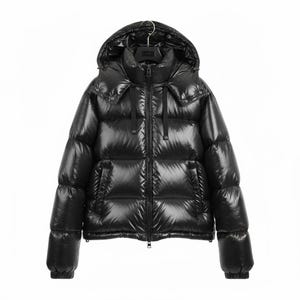 Puede incluir: Una chaqueta acolchada negra brillante con capucha. La chaqueta tiene un cuello alto, cierre de cremallera y dos bolsillos laterales. La chaqueta está colgada de una percha negra sobre un fondo blanco. La chaqueta está diseñada para el frío.