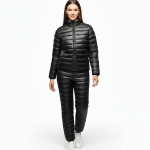 May include: A black quilted puffer jacket and matching pants set. The jacket has a stand-up collar and a full-length zipper. The pants are a straight-leg style. The model is wearing white sneakers.