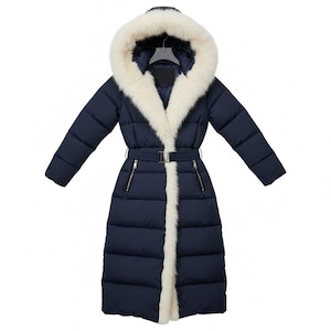 May include: A navy blue, full-length winter coat with a cream-colored fur-lined hood and trim. The coat features a belted waist, zipper pockets, and a quilted design. The coat is designed to provide warmth and protection from the elements.