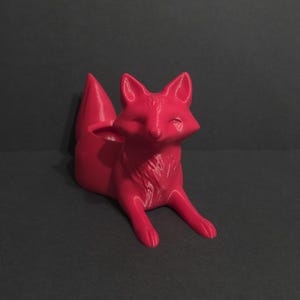 May include: A vibrant red fox-shaped planter. The fox is in a seated position with its front paws extended. The planter has a hollowed-out area on its back for holding small plants or decorative items. The fox has detailed facial features.