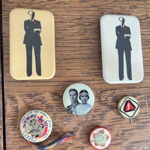 Op de afbeelding: Een verzameling van zes vintage spelden, waaronder twee rechthoekige badges met een man in een pak, een ronde speld met een koninklijk paar, een ronde badge met de tekst Long Live The King Vive Le Roi Canada 1939, een driehoekig embleem en een kleine ronde bloemenspeld.