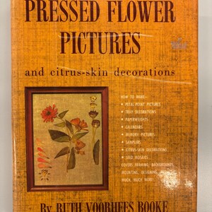 May include: A vintage book titled "PRESSED FLOWER PICTURES" with the subtitle "and citrus-skin decorations." The cover is orange with brown text and features a framed floral arrangement. The author's name is Ruth Voorhees Booke.
