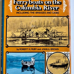 Könnte beinhalten: Ein gebundenes Buch mit dem Titel Ferryboats on the Columbia River Including the Bridges and Dams von Robert H. Ruby und John A. Brown. Der orangefarbene Einband zeigt ein großes historisches Schwarz-Weiß-Foto einer Fähre.
