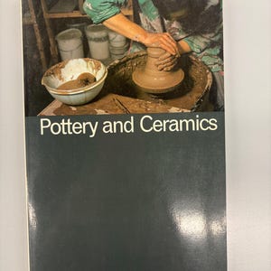 Op de afbeelding: Een boek getiteld "The Thames and Hudson Manual of Pottery and Ceramics" met een afbeelding van een pottenbakker aan het werk. De omslag is donkergroen met witte tekst. Door David Hamilton.