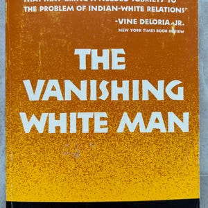 以下が含まれることがあります： スタン・スタインナー著「The Vanishing White Man」というタイトルの本。表紙はオレンジと黄色のグラデーションの背景に白い文字で書かれています。ヴァイン・デロリア・ジュニアの引用も含まれています。