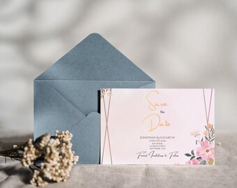 May include: A wedding invitation suite featuring a pale pink card with gold script that reads "Save the Date." The card is decorated with watercolor flowers and geometric lines. A blue envelope and dried flowers are also present.