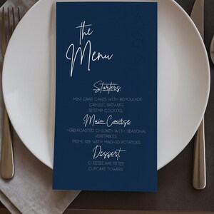 Peut inclure: Un menu bleu marine avec du texte blanc manuscrit, posé sur une assiette blanche avec des couverts. Le menu propose des entrées, un plat principal et des desserts. Le texte comprend "the Menu", "Starters", "Main Course", et "Dessert".