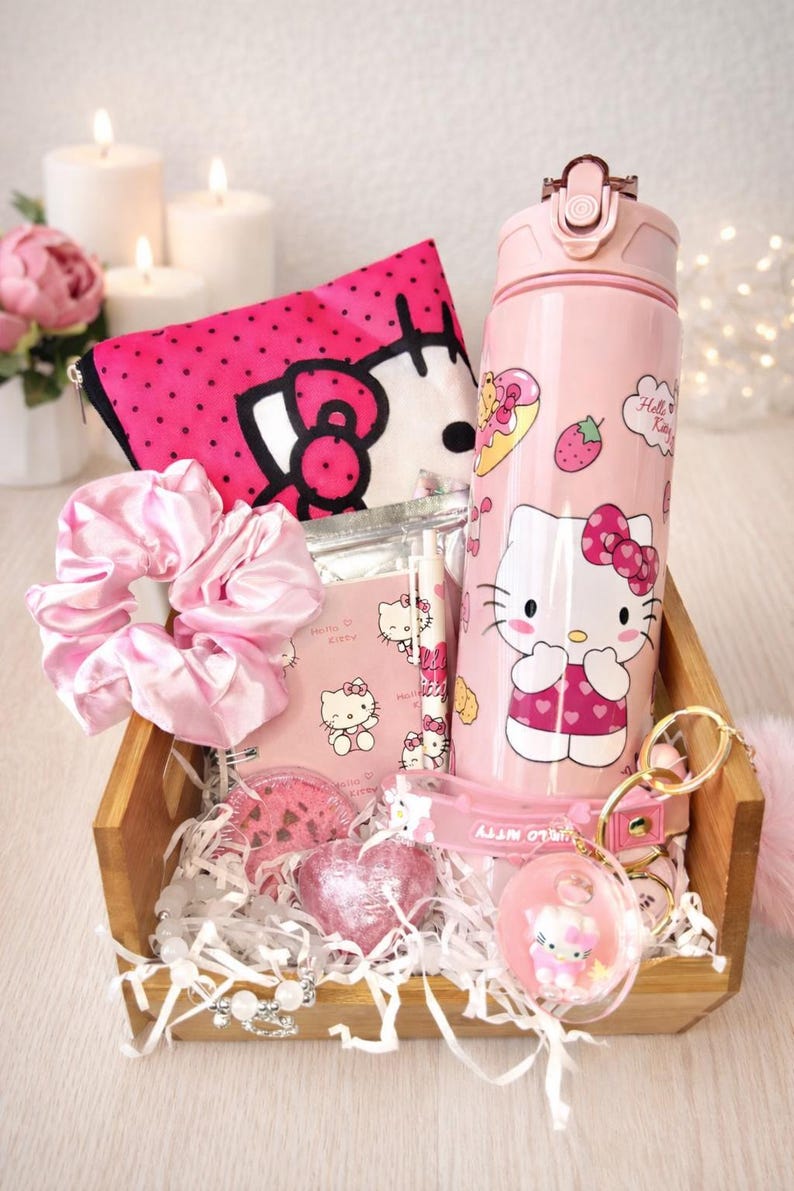 May include: A wooden crate filled with pink Hello Kitty themed items. Includes a water bottle, cosmetic bag, scrunchie, stationery, bath bombs, and a keychain. The water bottle has a Hello Kitty graphic and is approximately 25 cm tall.