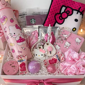 May include: A gift box containing Hello Kitty merchandise. It features a pink water bottle, a pink polka dot pouch, a bracelet, a keychain, a notepad, sweets, bath bombs, and a pink satin scrunchie. The box is tied with a pink ribbon.