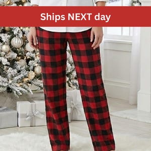 May include: Red and black buffalo plaid pajama pants. The pants are paired with a white button-down shirt. The image is set in front of a Christmas tree and wrapped gifts.