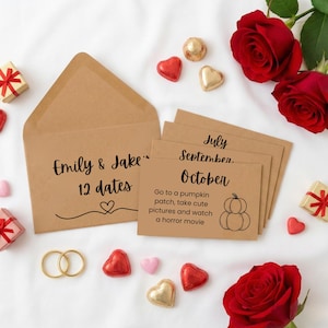 May include: A kraft paper envelope and date cards with the text "Emily & Jake" and "12 dates". The October card suggests a pumpkin patch and a horror movie. Red roses, heart-shaped candies, and small gifts are scattered around.