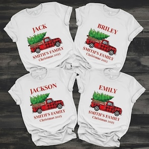 May include: White t-shirts with a Christmas theme. Each shirt features a red plaid truck carrying a green Christmas tree, with the name "Jack", "Briley", "Jackson", or "Emily" above and "Smith's Family Christmas 2025" below.