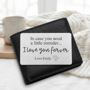 Op de afbeelding: Zwart leren portemonnee met een zilveren kaartinzet. De kaart heeft de tekst "In case you need a little reminder... I love you forever Love Emily" in zwart schrift. Twee harten staan onderaan de kaart.
