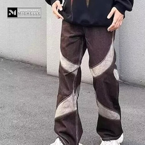 May include: Brown denim pants with light gray geometric panels. The pants have a relaxed fit and a unique design. The brand logo is visible in the top left corner. A modern take on a classic style.