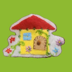 May include: A colourful felt house with a red roof, yellow walls, and a brown door. The house is decorated with embroidered flowers, green vines, and a blue window. The edges are white, set against a green background.