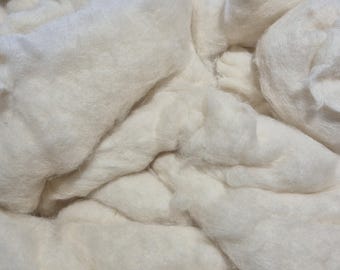以下が含まれることがあります： 柔らかくふわふわしたオフホワイトの綿の詰め物の山をクローズアップ。素材は束ねられており、さまざまな深さと影のあるテクスチャのある表面を作り出しています。綿はきれいで、工芸品やテキスタイルに使用できるようです。