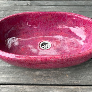 May include: A deep red oval ceramic sink with a silver drain.