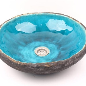 May include: A turquoise ceramic sink with a rough, textured exterior and a smooth, glossy interior. The sink has a round shape and a drain in the center.